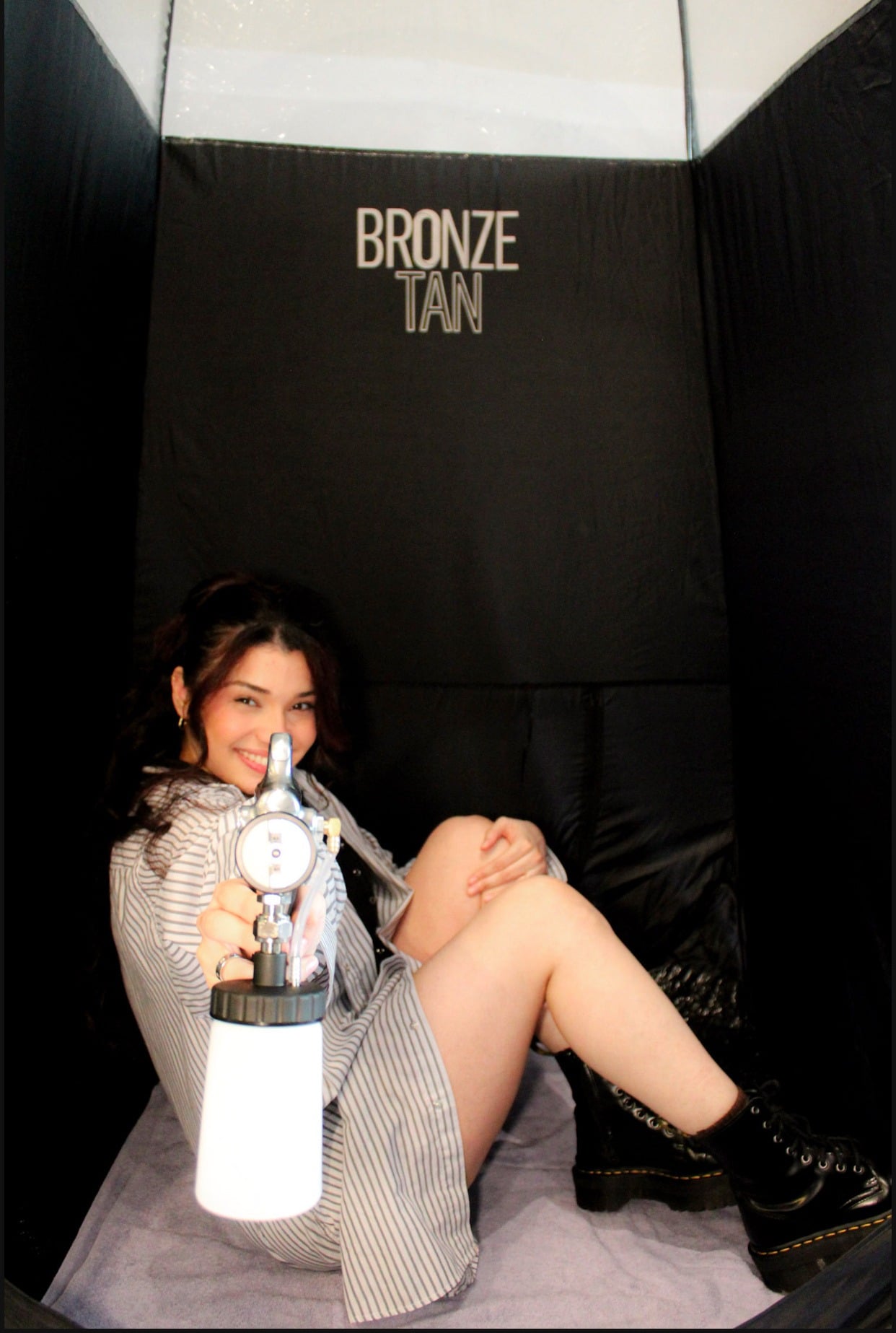 Estefany Costa holding spray tan equipment inside a mobile tanning tent