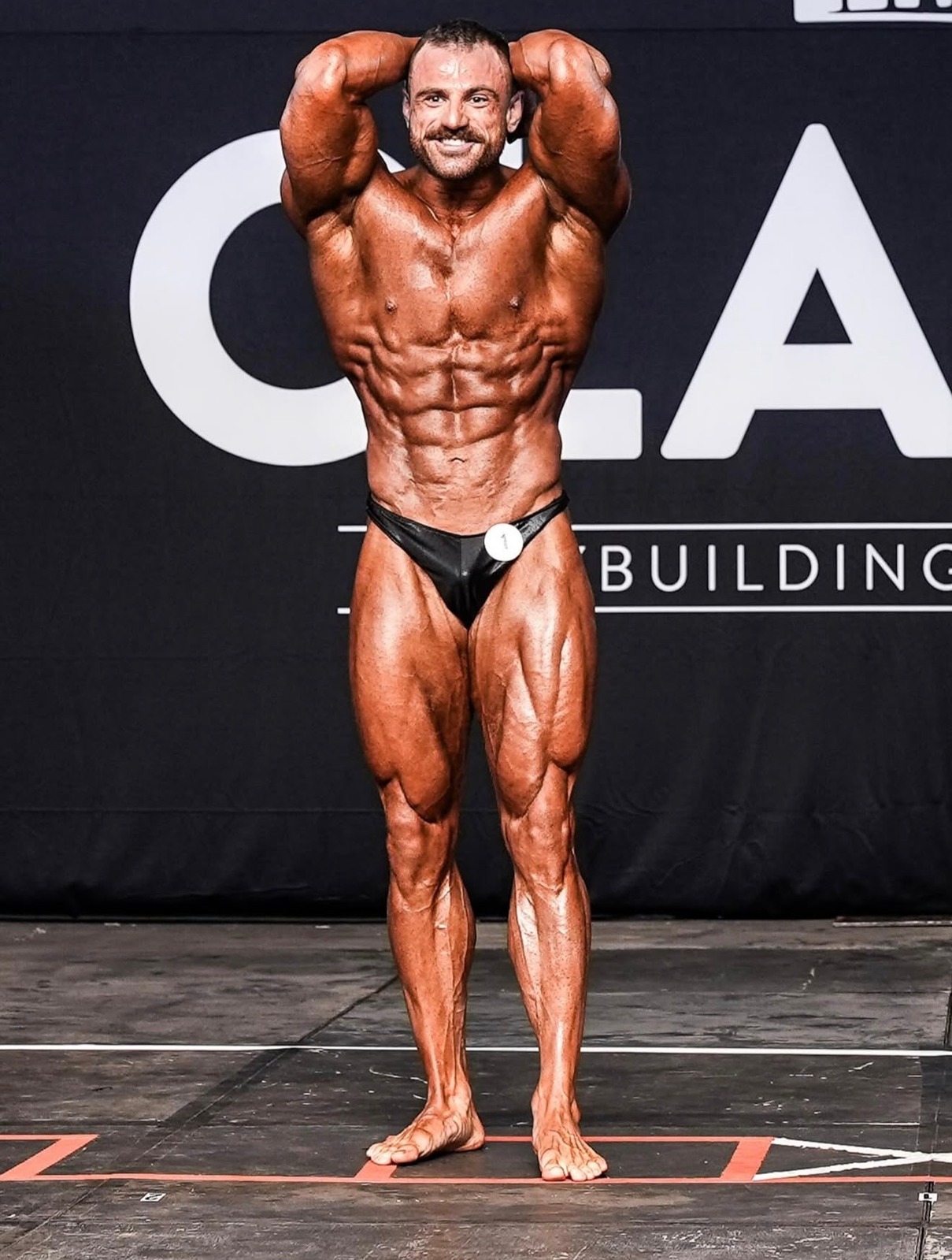 Male bodybuilder posing on stage with competition tan color